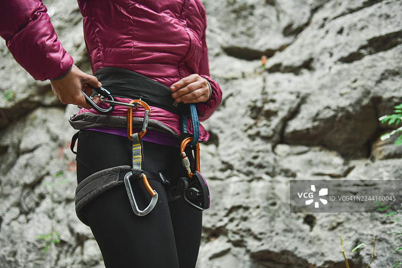身穿粉色羽绒服、头戴头盔、身系安全带的女性登山者在岩石户外悬崖峭壁上图片素材