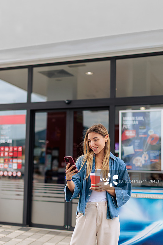 加油站里，一位女士一边喝咖啡一边使用手机图片素材