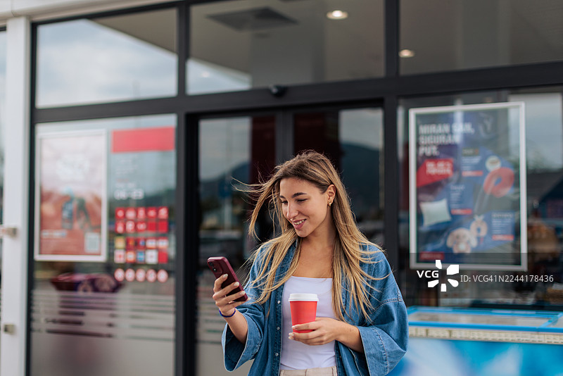 女子在加油站用手机喝咖啡图片素材