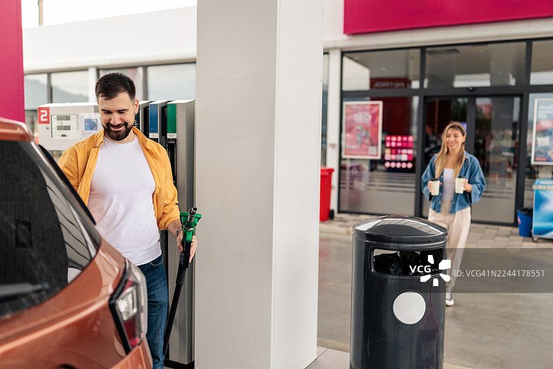女士在男士给汽车加油时送上咖啡图片素材