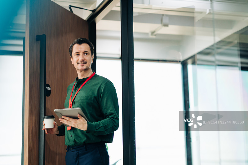 自信的商人在办公室门口拿着平板电脑和咖啡杯图片素材