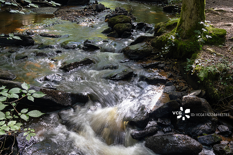 从高处俯瞰，瀑布倾泻而下，流过郁郁葱葱的绿色森林中覆盖着苔藓的岩石，水流呈现长曝光效果。图片素材