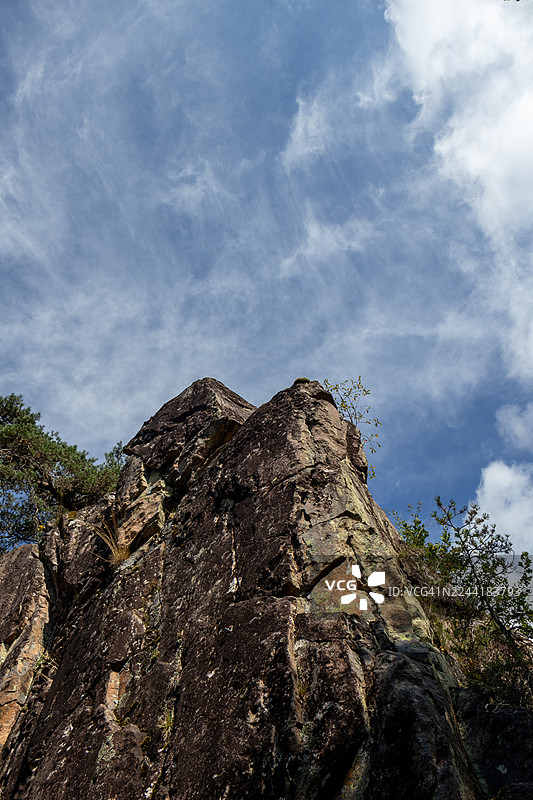 雄伟的岩石构造，从低角度仰望，直指布满缕缕云彩的戏剧性蓝色天空图片素材