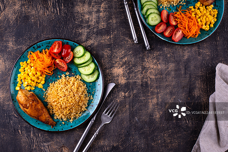 深色木桌上摆放着鸡肉、保加利亚小米和新鲜蔬菜组成的健康均衡餐图片素材