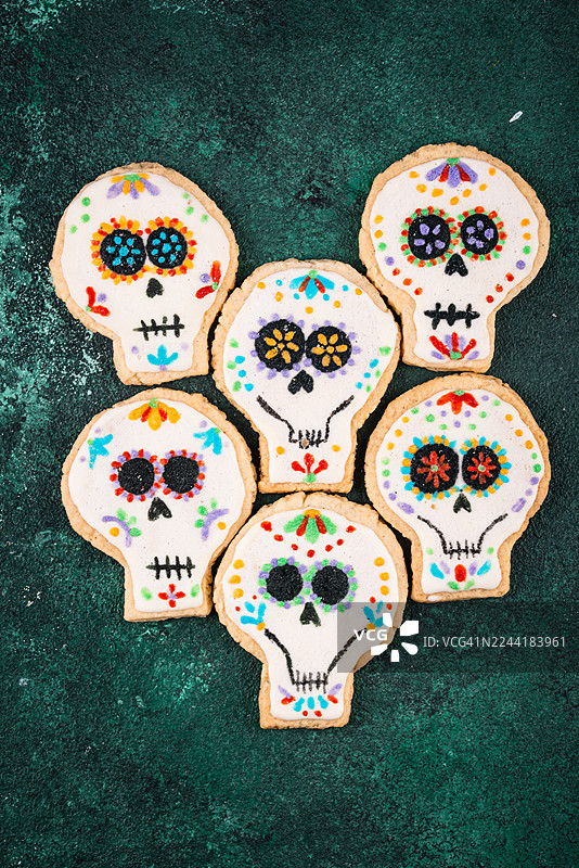 俯视视角拍摄的彩色糖骷髅饼干，背景为深绿色纹理，庆祝亡灵节图片素材