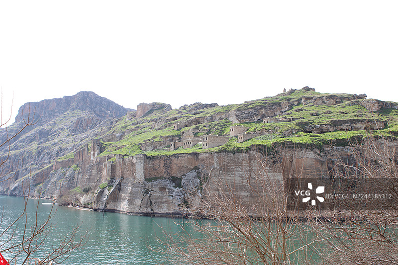 清澈天空下，宁静的河流缓缓流过古老的悬崖民居和郁郁葱葱的绿色山峦，构成一幅风景画。图片素材