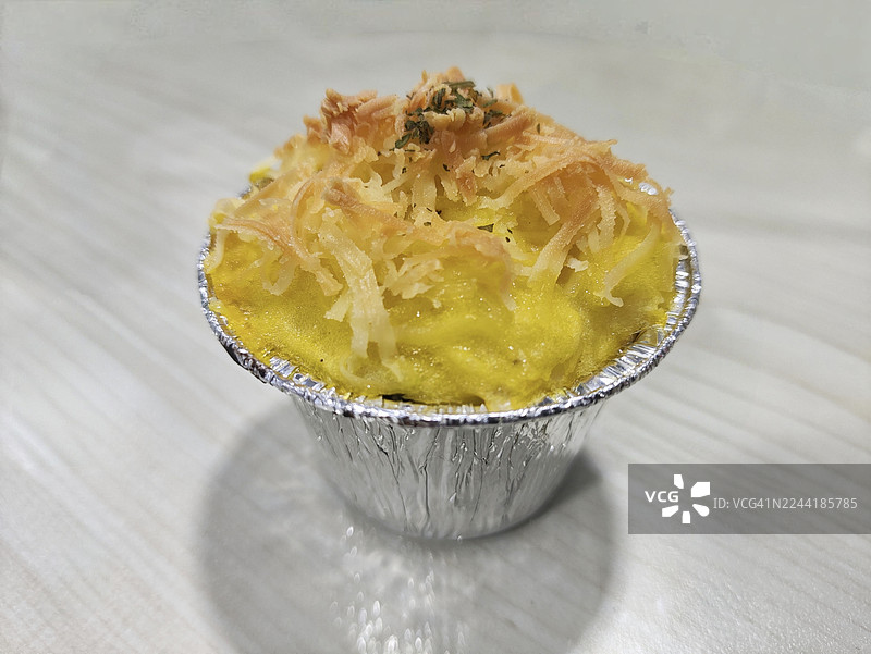 美味的烤芝士通心粉装在铝箔杯中，摆放在浅色木桌上图片素材