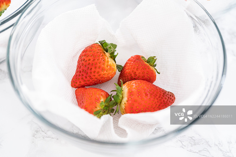 刚洗好的草莓在白色大理石台面上的玻璃碗中沥干水分，准备进行下一步处理图片素材