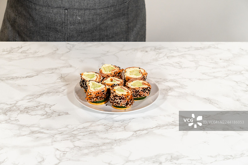 白盘上美味的鲑鱼奶油芝士卷配芝麻，放在大理石桌上，准备上菜图片素材
