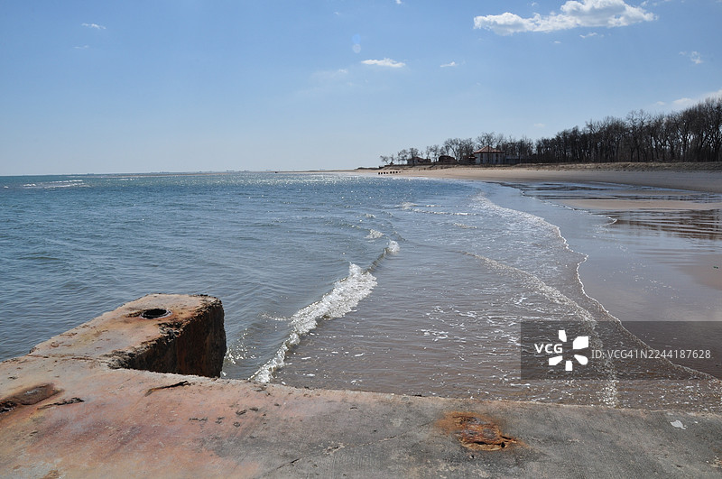 中国北戴河，晴朗蓝天下，宁静海岸景色，温柔的海浪拍打着沙滩，前景中是混凝土码头图片素材