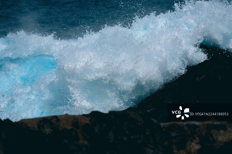 海浪拍打着黑色岩石，蓝色的泡沫飞溅 | 海浪蓝色的泡沫飞溅图片素材