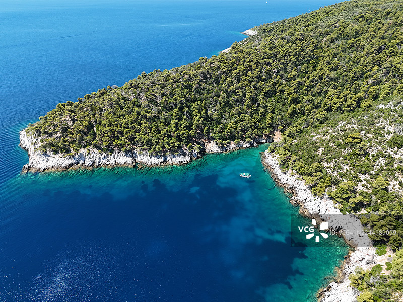 从高处俯瞰，郁郁葱葱的绿色海岸线，清澈碧绿的海水和一艘小船，营造出夏日宁静的氛围。图片素材