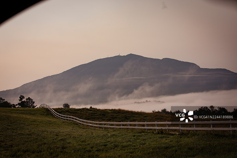 日出时分，白雪皑皑的栅栏和绿色的田野笼罩在薄雾中的宁静山景，美国东伯克。图片素材