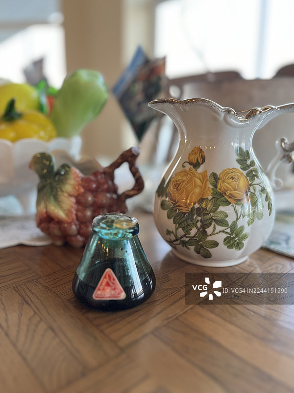 木桌上，带有黄色玫瑰和其他装饰品的仿古陶瓷水罐特写图片素材
