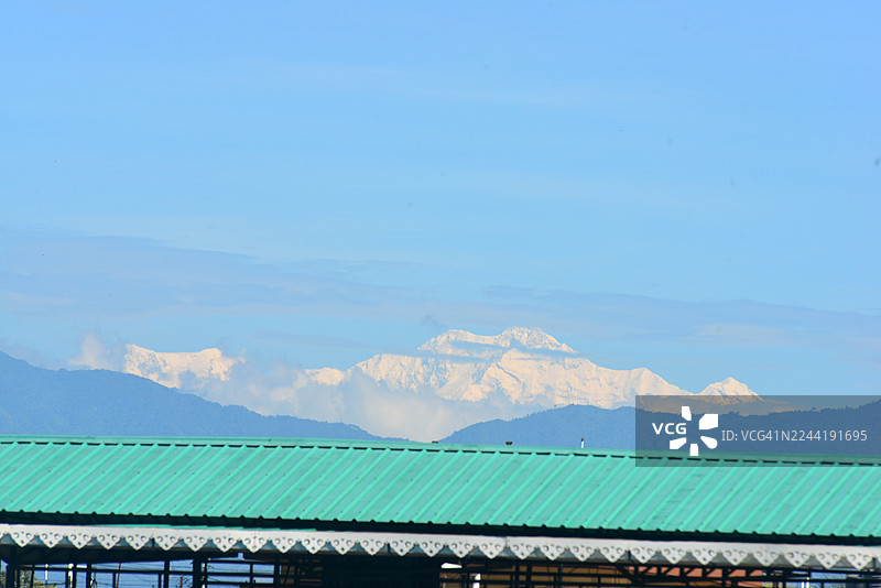 雪山巍峨，喜马拉雅山脉在湛蓝的天空下格外壮丽，前景中是绿色的屋顶，位于印度西里古里。图片素材
