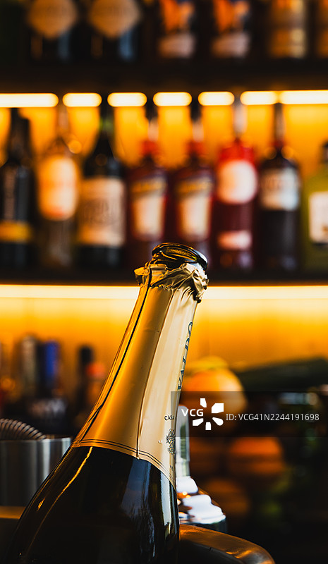 吧台上的起泡酒瓶特写，瓶身覆有金色锡箔，背景是模糊的酒瓶图片素材