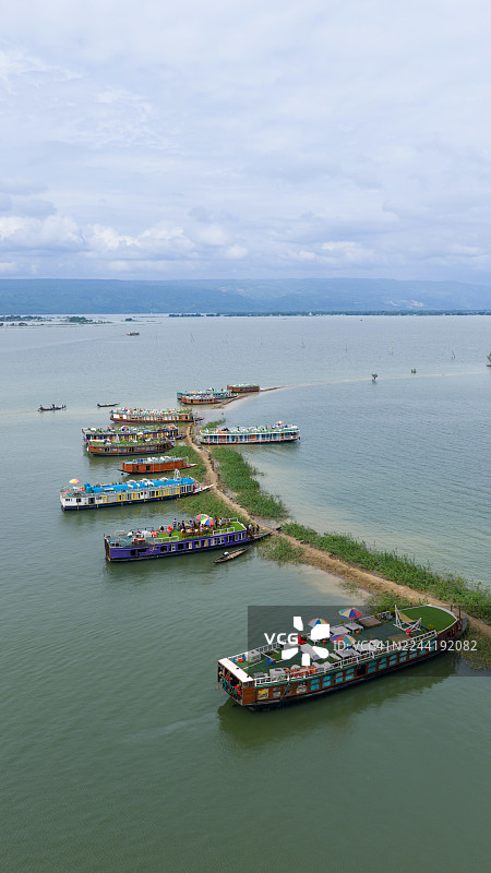 从空中俯瞰，在阴沉的天空下，狭长陆地上停靠着一排排船屋，它们被广阔的水域所环绕。图片素材