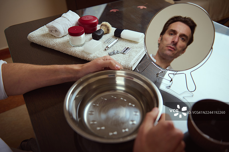 男人在梳妆台前，旁边放着一套理容工具，圆镜中映照出他的脸图片素材