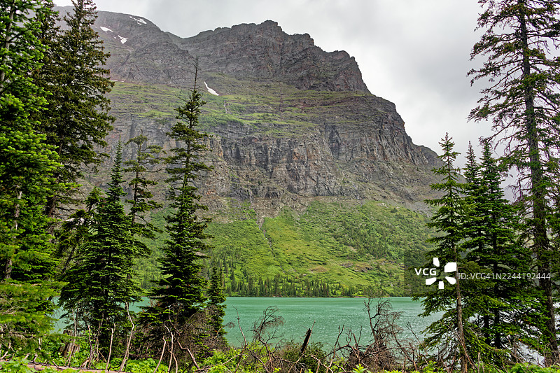 宁静的山间湖泊，四周环绕着郁郁葱葱的绿树和崎岖多云的山景，位于美国东冰川公园 Josephine Lake S Shore Josephine Lake Trl。图片素材