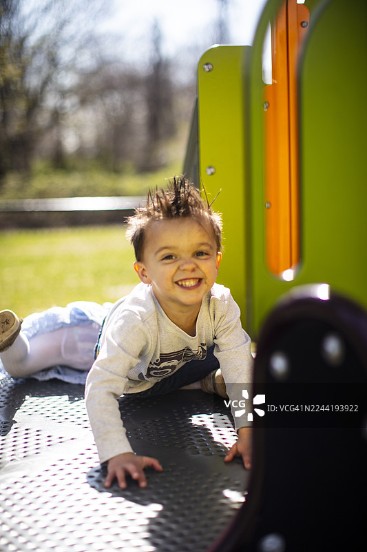 阳光明媚的日子里，一个快乐的小男孩在色彩鲜艳的游乐场上玩耍，对着镜头微笑图片素材