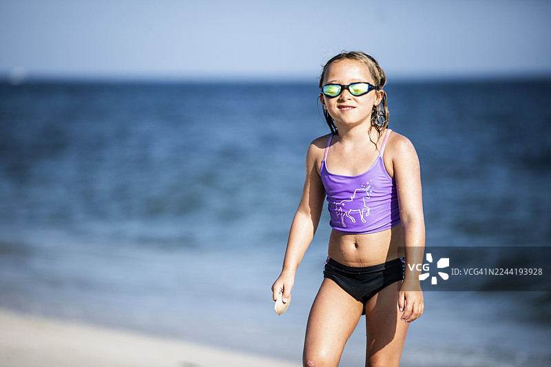 穿着泳衣和泳镜的年轻女孩站在海边沙滩上，面带微笑看向镜头图片素材