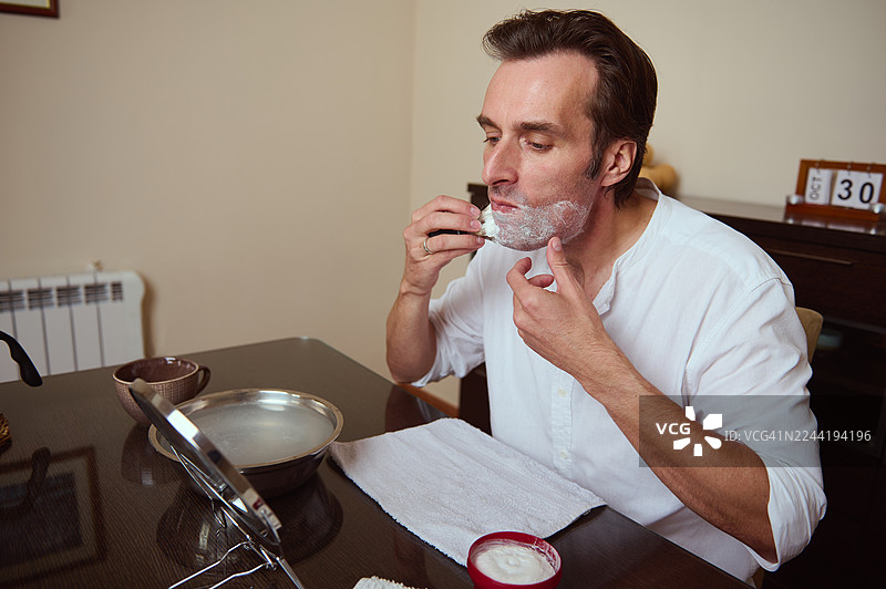 在家刮胡子的男人：早晨用剃须膏和镜子反射的日常图片素材