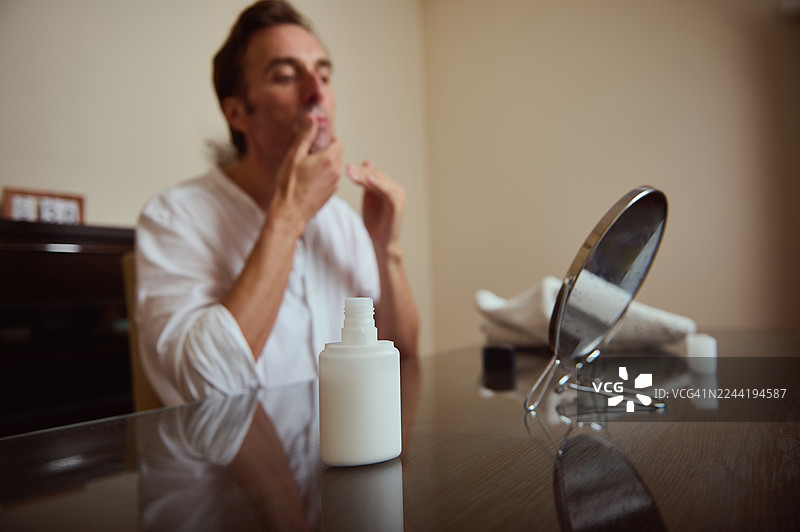 男人在梳妆台前进行护肤，旁边有瓶子、镜子和宁静的氛围图片素材