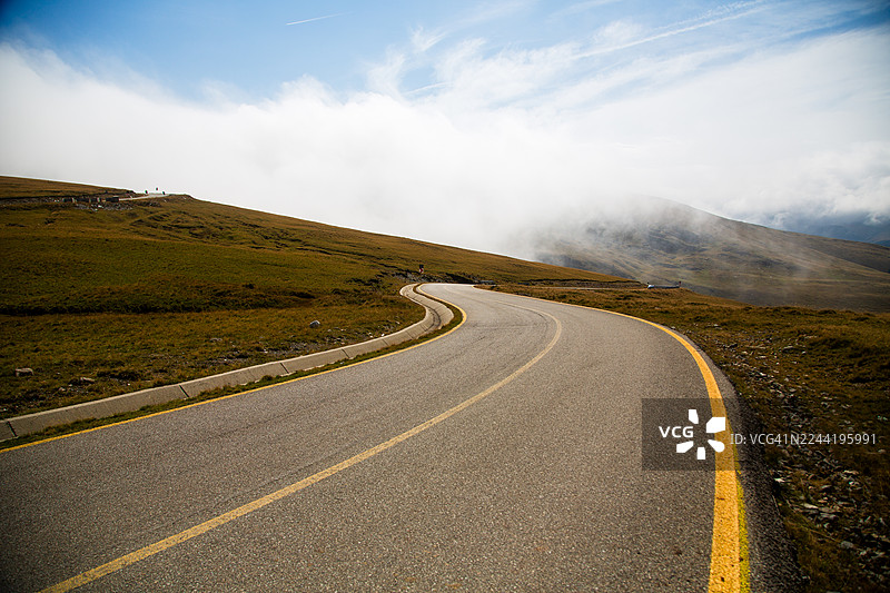 蜿蜒的道路穿过广阔的绿色山地景观，头顶是多云的天空，唤起了旅程和冒险的感觉，罗马尼亚，特兰萨尔皮纳公路图片素材