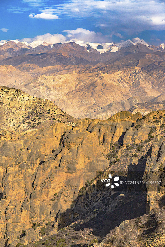 雄伟的喜马拉雅山脉风光，拥有高耸的山峰、崎岖的山谷以及点缀着零星云彩的鲜艳蓝天，地点为尼泊尔木斯塘的洛曼塘。图片素材