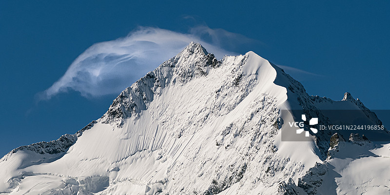 湛蓝晴朗的天空下，雄伟的雪山峰顶伴着缕缕白云，展现出崎岖之美与辽阔壮丽图片素材