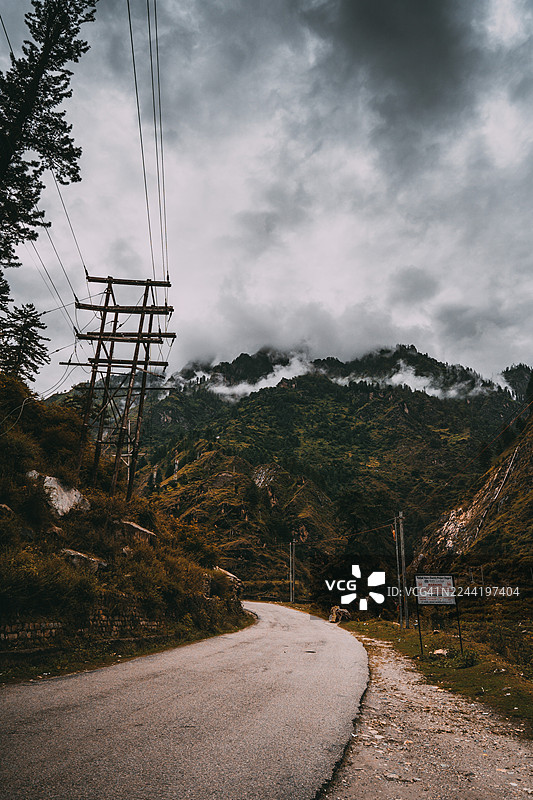 蜿蜒的山路，架设着电线，天空布满戏剧性的云彩，地点：马尼卡兰，印度，卡索尔山丘图片素材