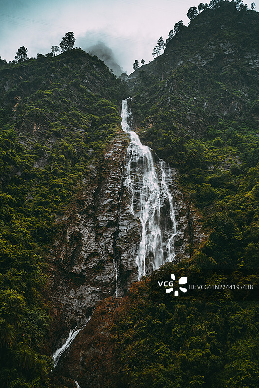 印度卡索尔山马尼卡兰，壮丽的瀑布从郁郁葱葱的绿色山坡上倾泻而下，天空戏剧般地变幻着图片素材