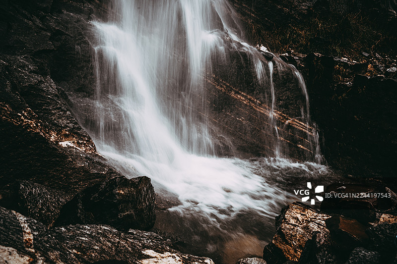 印度马纳利森林中，壮丽的瀑布飞流直下，倾泻在黝黑的岩石上，长曝光摄影图片素材