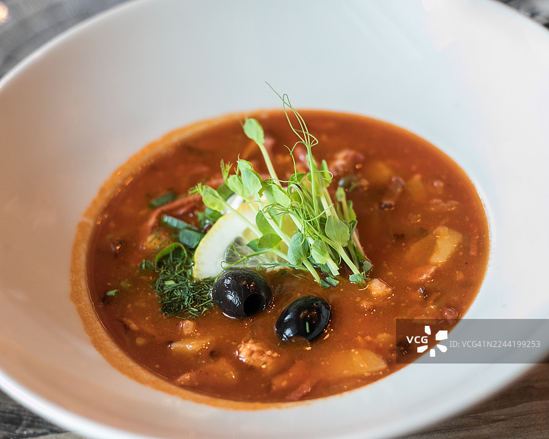 一碗色彩鲜艳的汤，配以新鲜香草、柠檬和橄榄，盛放在质朴的桌子上，特写镜头图片素材