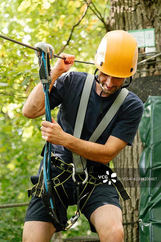 身着安全带和头盔的男子在郁郁葱葱的绿色森林中进行高空绳索挑战图片素材