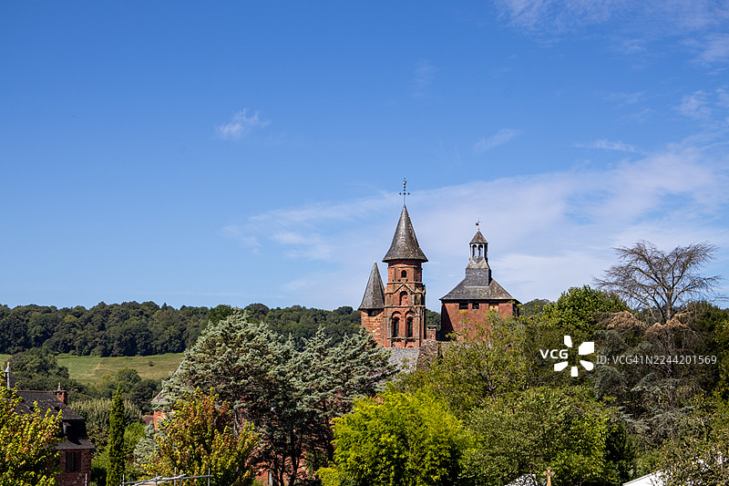 法国康塔尔地区，在明亮的蓝天下，历史悠久的教堂塔楼矗立在郁郁葱葱的绿色景观之上，展示着中世纪的建筑风格。图片素材