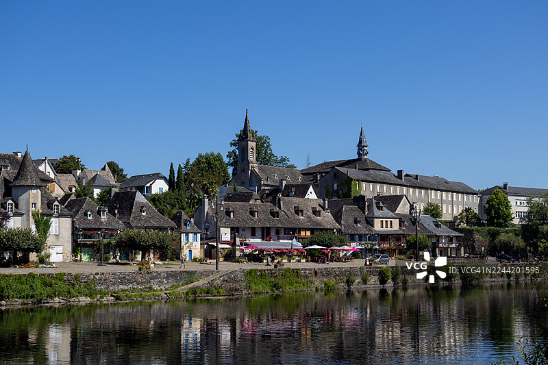 法国康塔尔省，风景如画的欧洲村庄，宁静的河流倒映着历史建筑，天空湛蓝图片素材