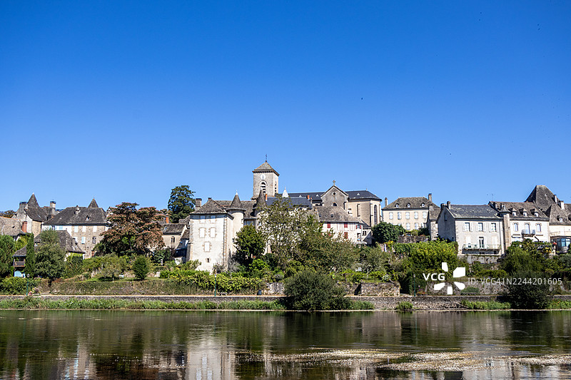 法国康塔尔地区，一座历史悠久的欧洲村庄，古老的建筑依偎在宁静的河流旁，在湛蓝的天空下，倒影映入水中。图片素材