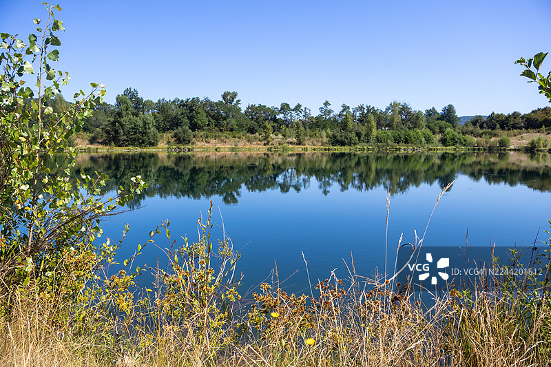 阳光明媚的一天，宁静的湖面倒映着湛蓝的天空和繁茂的绿树，法国，康塔尔图片素材