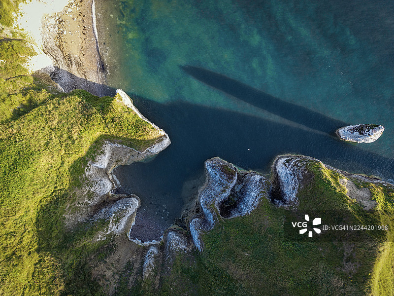 崎岖海岸线的空中俯瞰图，有绿色悬崖、岩石海滩、清澈的绿松石海水和一个小海蚀柱图片素材