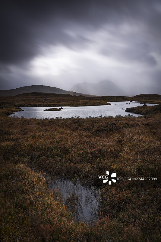 从苏格兰格伦科一座雄伟崎岖的山峰俯瞰宁静的秋日景色，金黄的秋叶与变幻的天空交相辉映。图片素材