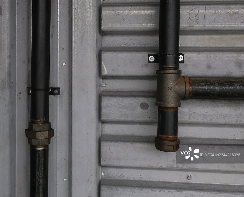 金属墙上的两根管道，一根是直的，另一根带有三通接头图片素材
