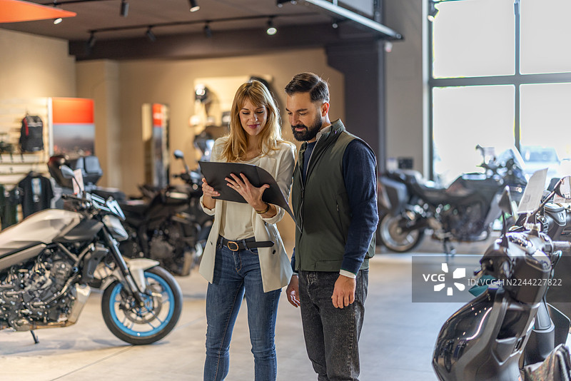 商业伙伴在摩托车展厅审阅平板电脑的详细信息，以进行销售和协作图片素材