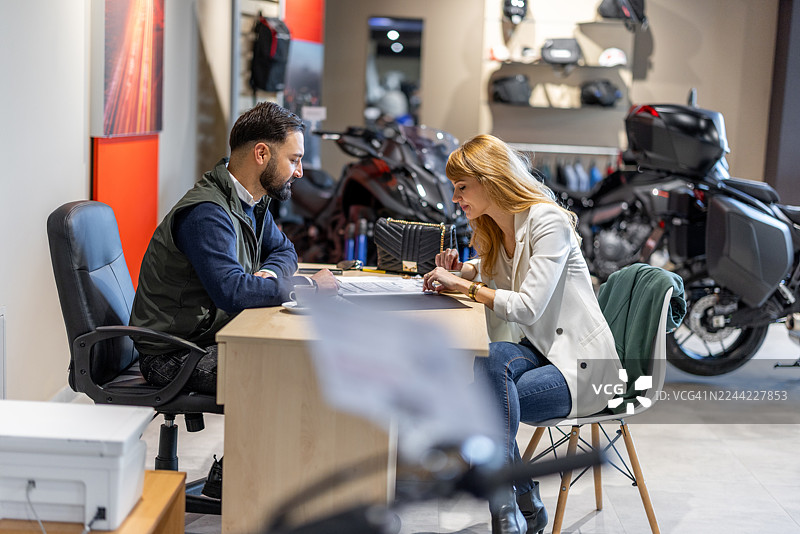 在摩托车展厅里，一位男士和一位女士正在讨论文件，进行商务会议图片素材