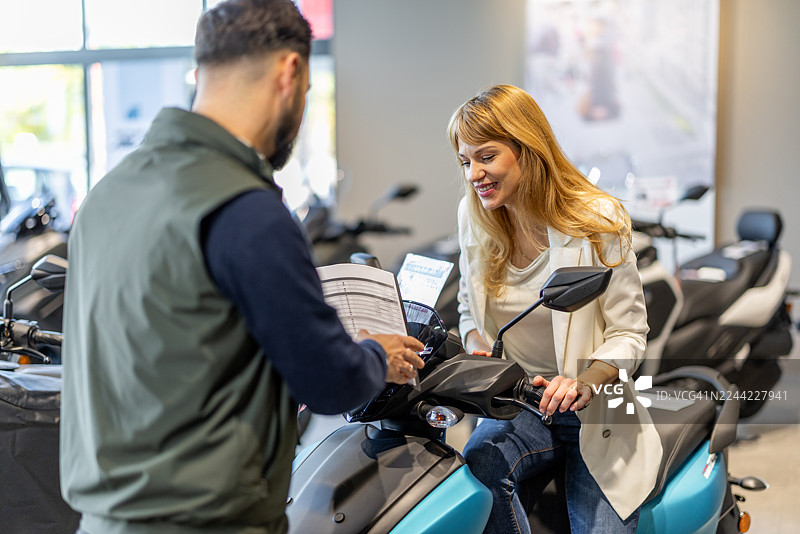 一对友好的夫妇在现代摩托车展厅与销售人员讨论购买踏板车图片素材