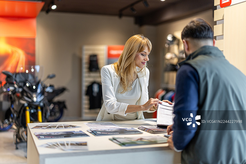 专业女销售顾问在摩托车展厅协助顾客查阅宣传册图片素材
