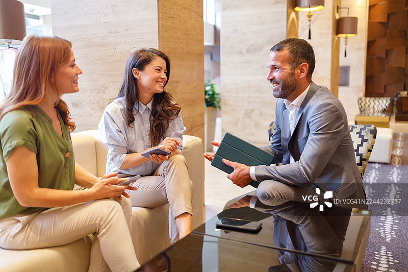 商务同事们在现代办公室大堂举行非正式会议，用数码平板和智能手机讨论工作图片素材