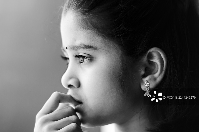 一位沉思的印度小女孩的黑白肖像，她带着温柔的微笑，目光专注地望向光亮处。图片素材