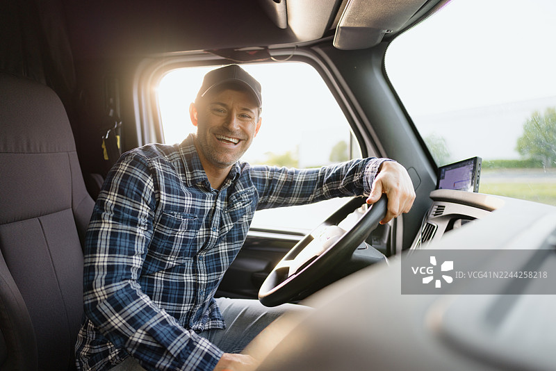 微笑的卡车司机坐在驾驶室里的肖像图片素材