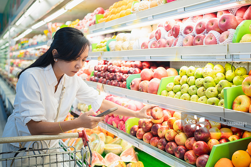 女子在超市用智能手机比较水果价格图片素材